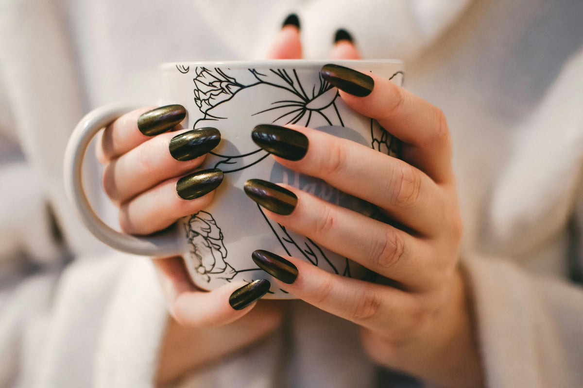 Mains avec manucure foncée tenant une tasse, mise en valeur des ongles soignés - Cosmesud